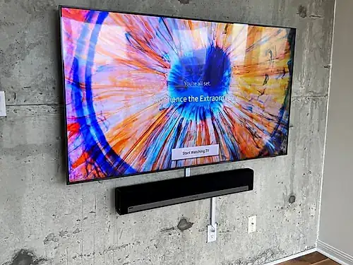 TV and soundbar mounted on a bare concrete loft wall, with the cable run dropped in a slim conduit to the outlet