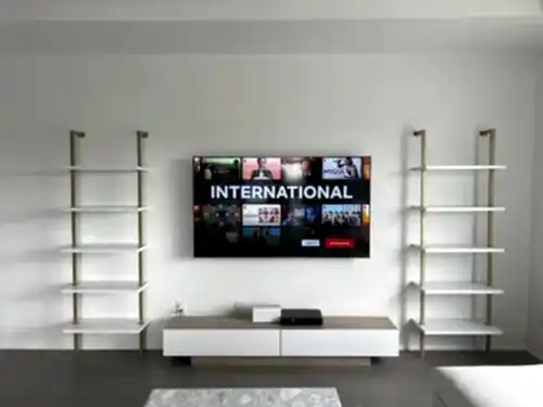 Flat screen mounted flush on a white wall between two brass ladder shelving units, with no visible cables