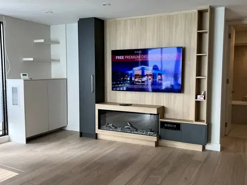 TV mounted on a light oak slat panel above a built-in linear electric fireplace in a condo living room