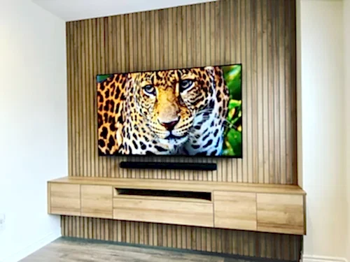 TV and soundbar mounted on a vertical wood slat feature wall above a long oak floating console