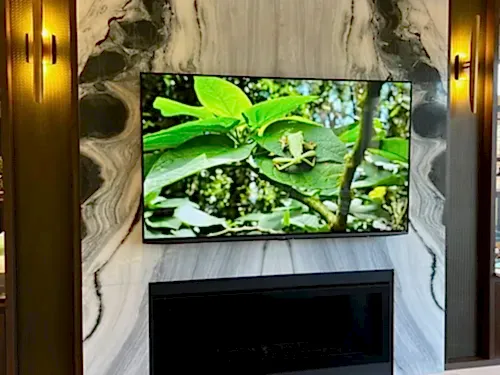 TV mounted on a book-matched marble fireplace surround above a linear insert, framed by wood and brass millwork