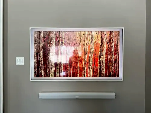 Samsung Frame TV in a white bezel showing birch forest artwork, with a white soundbar mounted below