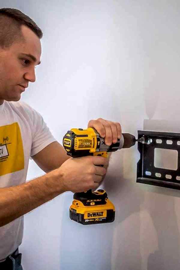 Installer levelling a TV wall mount bracket against a stud before fixing it