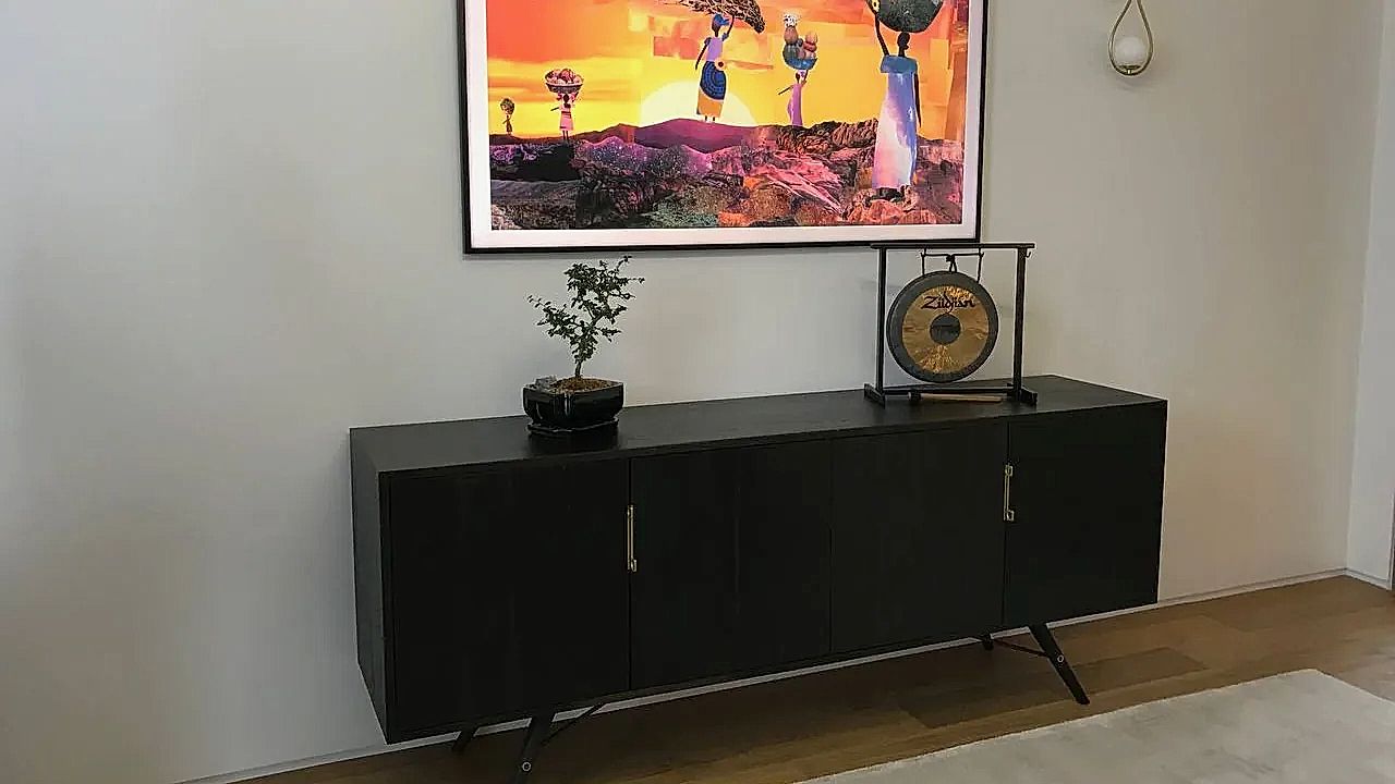 Samsung Frame TV in art mode above a black credenza, mounted flush on a plain wall
