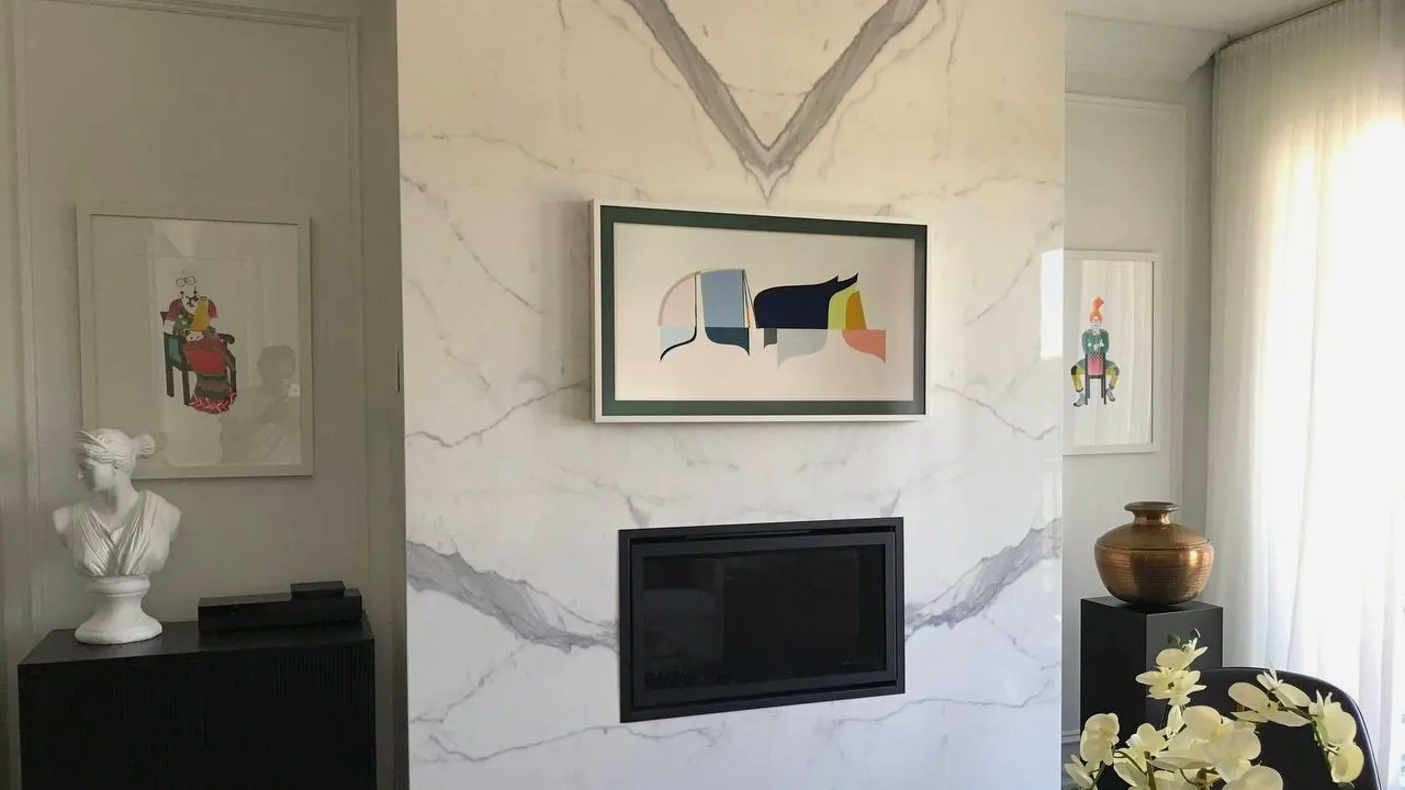 Samsung Frame TV with a white bezel mounted flush on a marble fireplace wall above a linear gas firebox