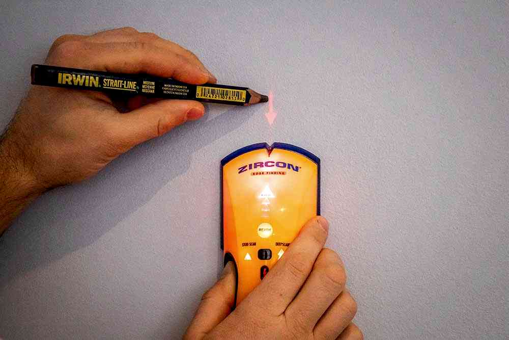Installer sweeping a wall with an electronic stud detector to confirm stud positions before marking a TV bracket
