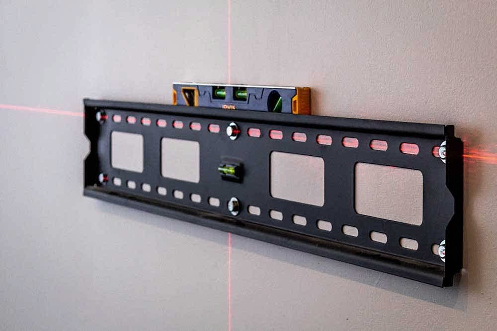 Installer checking a mounted TV bracket with a spirit level before fitting the screen