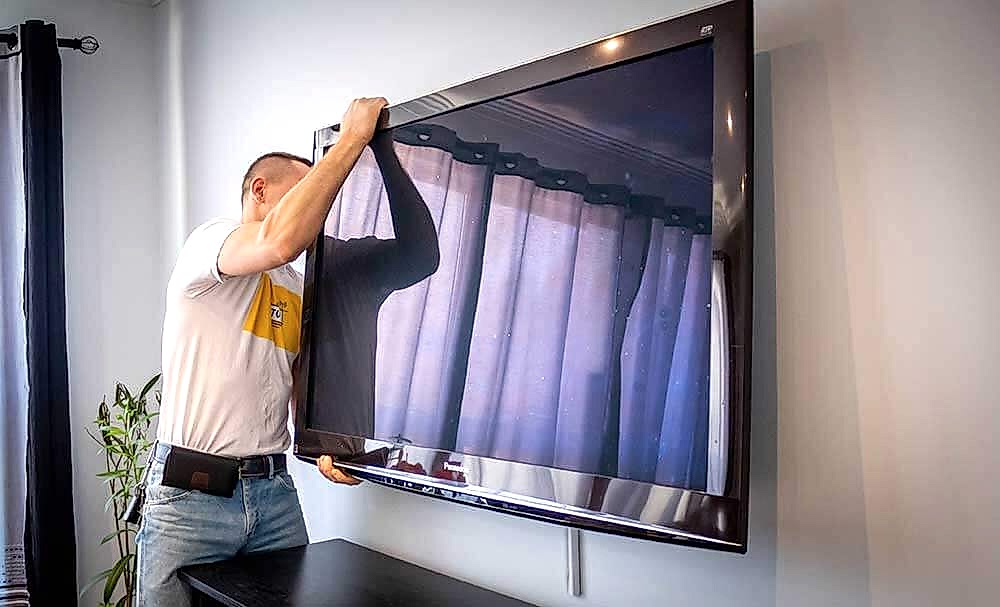 Two installers lifting a large flat-screen TV onto a wall bracket together