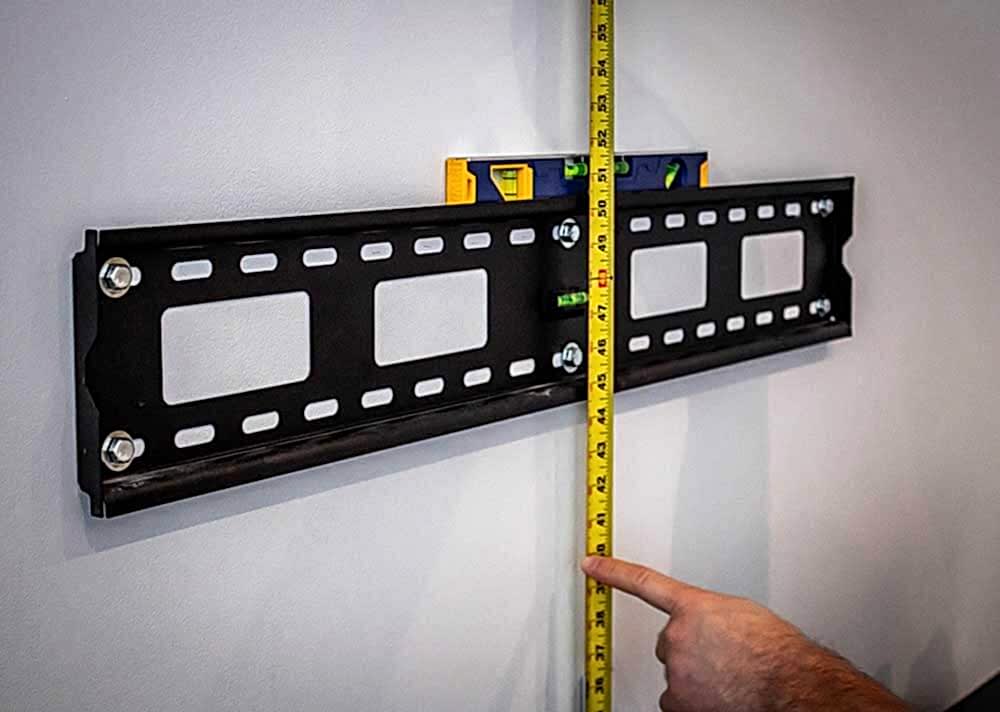 Installer measuring and marking the mounting height on a wall with a tape measure and pencil