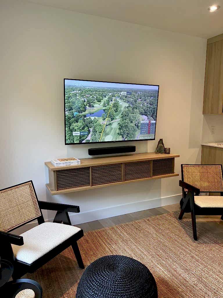 Soundbar resting on a floating wooden shelf beneath a wall mounted TV